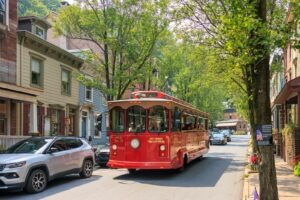 Red trolley car driving down a tree-lined street.